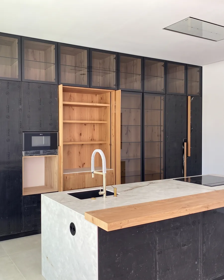 Cocina negra con vitrinas de cristal, armario de roble e isla con barra de madera